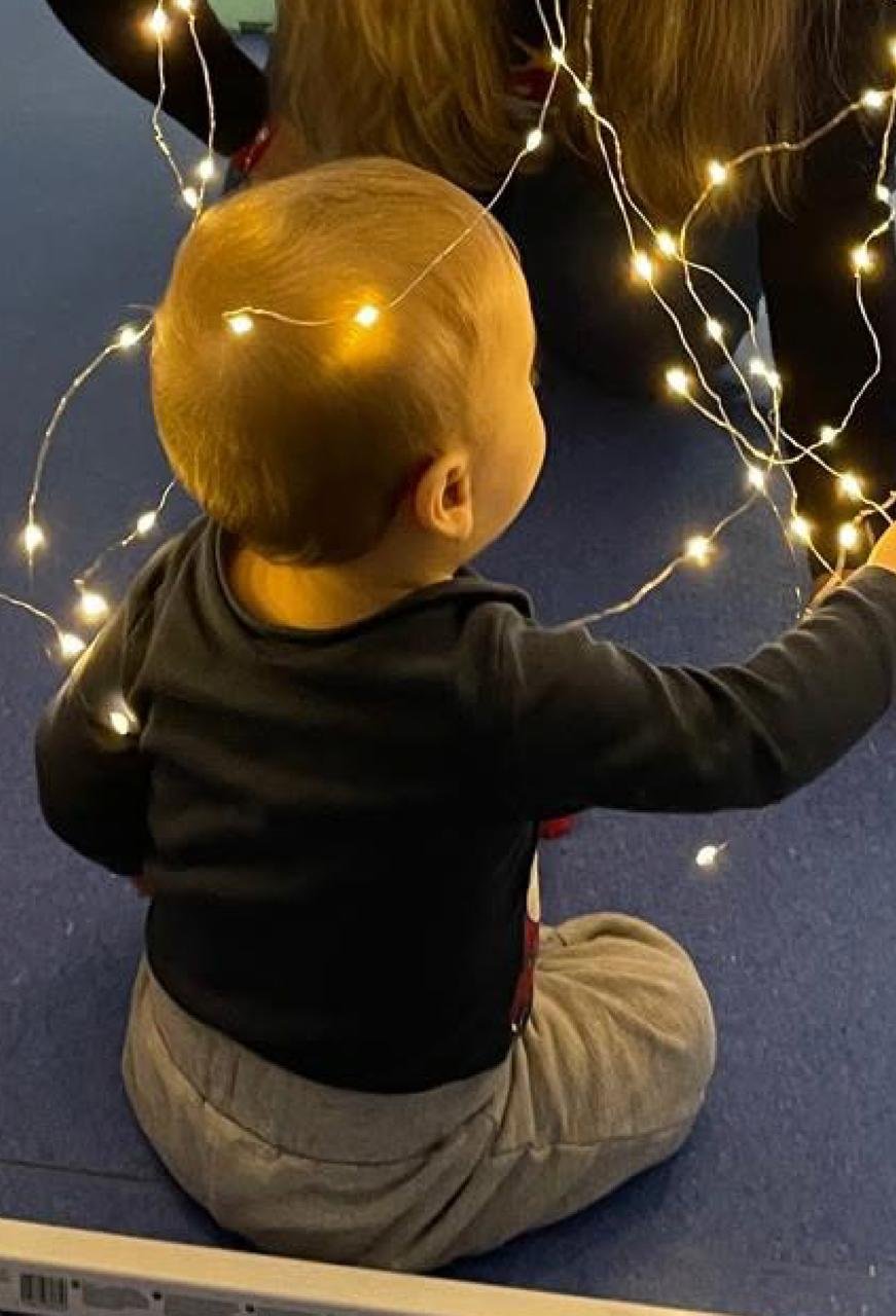 Bebé a explorar um fio de luzes com curiosidade, sentado no chão