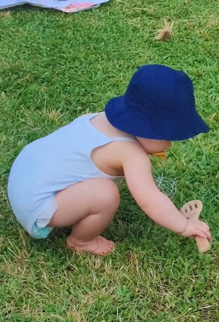 Criança agachada na relva, a explorar um objeto com as mãos