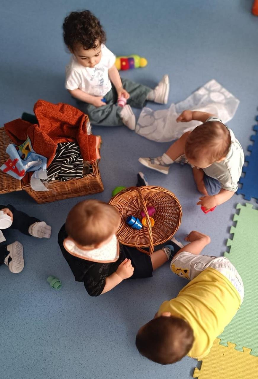 Grupo de crianças sentadas em roda a explorar cestos com brinquedos e tecidos